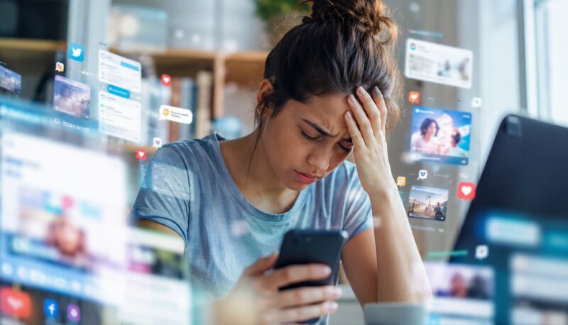 Žena drži telefon i deluje mentalno iscrpljeno, dok su oko nje prikazani brojni digitalni sadržaji, poruke i notifikacije koje simbolizuju preopterećenost informacijama